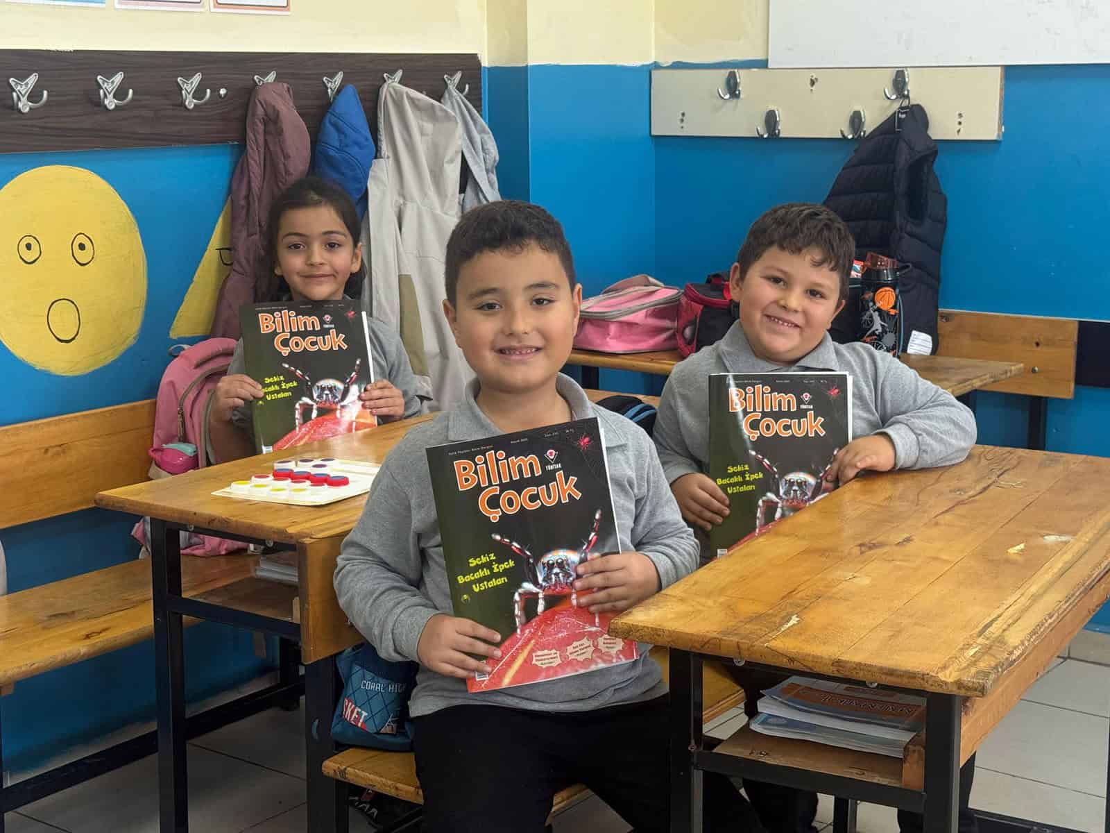 Sevimli çocuklar Bilim Çocuk kitabını tutarken kucaklarında gülümseyerek poz veriyor.